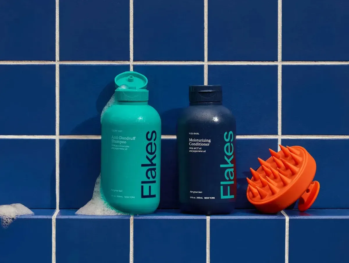 Flakes shampoo, conditioner, and scalp brush on blue tiles