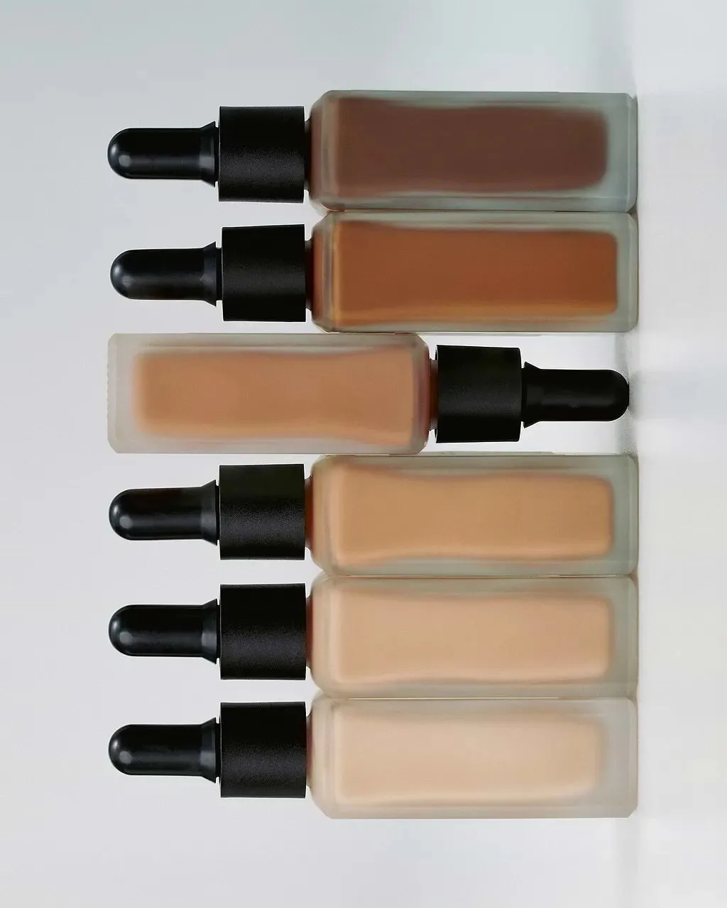 Six glass bottles of Typology Tinted Serum arranged by shade